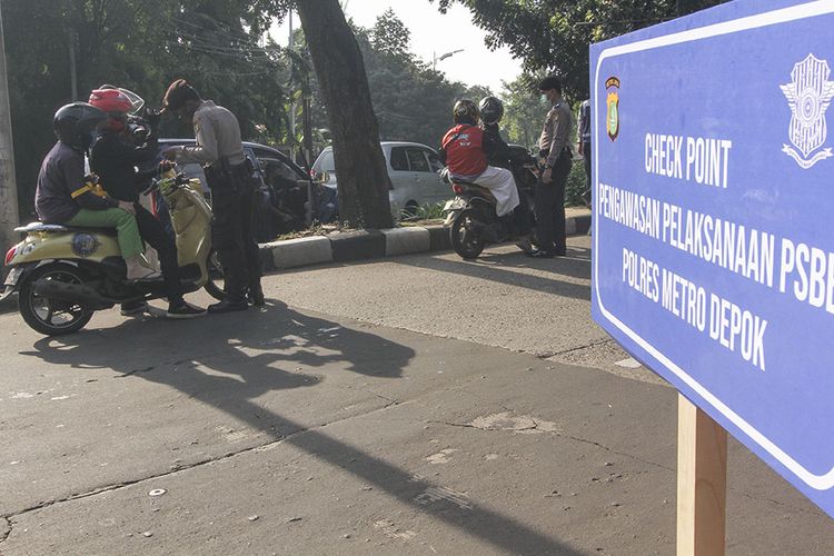 Petugas kepolisian memeriksa identitas pengendara motor yang berpenumpang saat penerapan PSBB di Perbatasan Jakarta - Depok, Depok, Jawa Barat, Rabu (15/4/2020). © Kompas