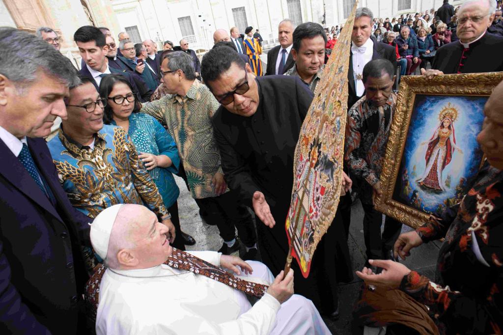 Paus Fransiskus dengan berselempang kain batik dari GKBRAy Adipati Paku Alam X menyaksikan Gunungan Wayang Kulit dari Sri Sultan Hamengku Buwono X saat Rm Markus Solo Kewuta SVD menjelaskan filosofi Gunungan dan di latar belakang lukisan Maria Bunda Segala Suku dari Uskup Agung Jakarta, Ignatius Kardinal Suharyo, di Basilica St. Petrus, Rabu (16/11/2022). (Foto: Istimewa) 